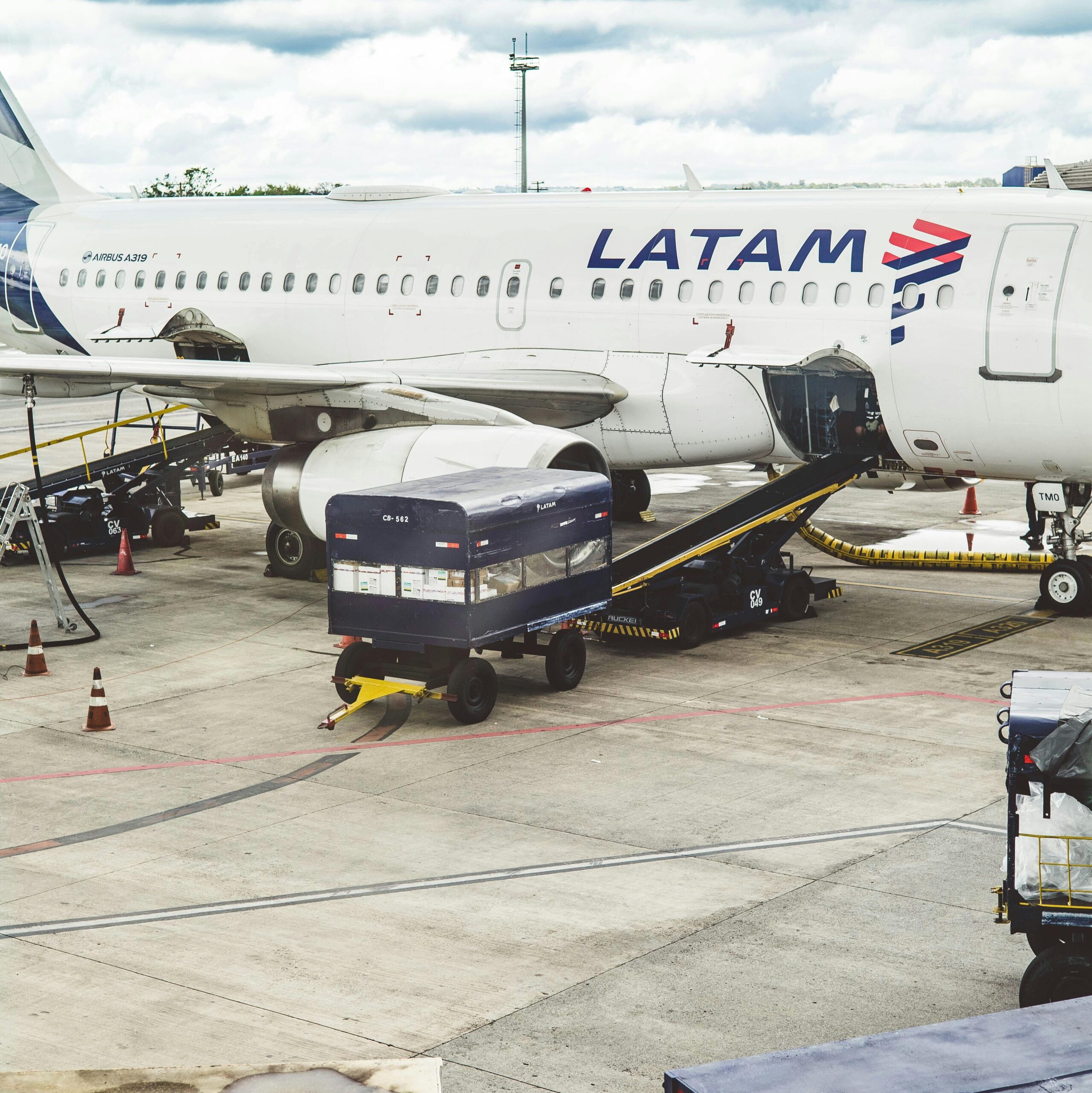 LATAM Airlines airplane being serviced at airport terminal with cloudy sky above.
